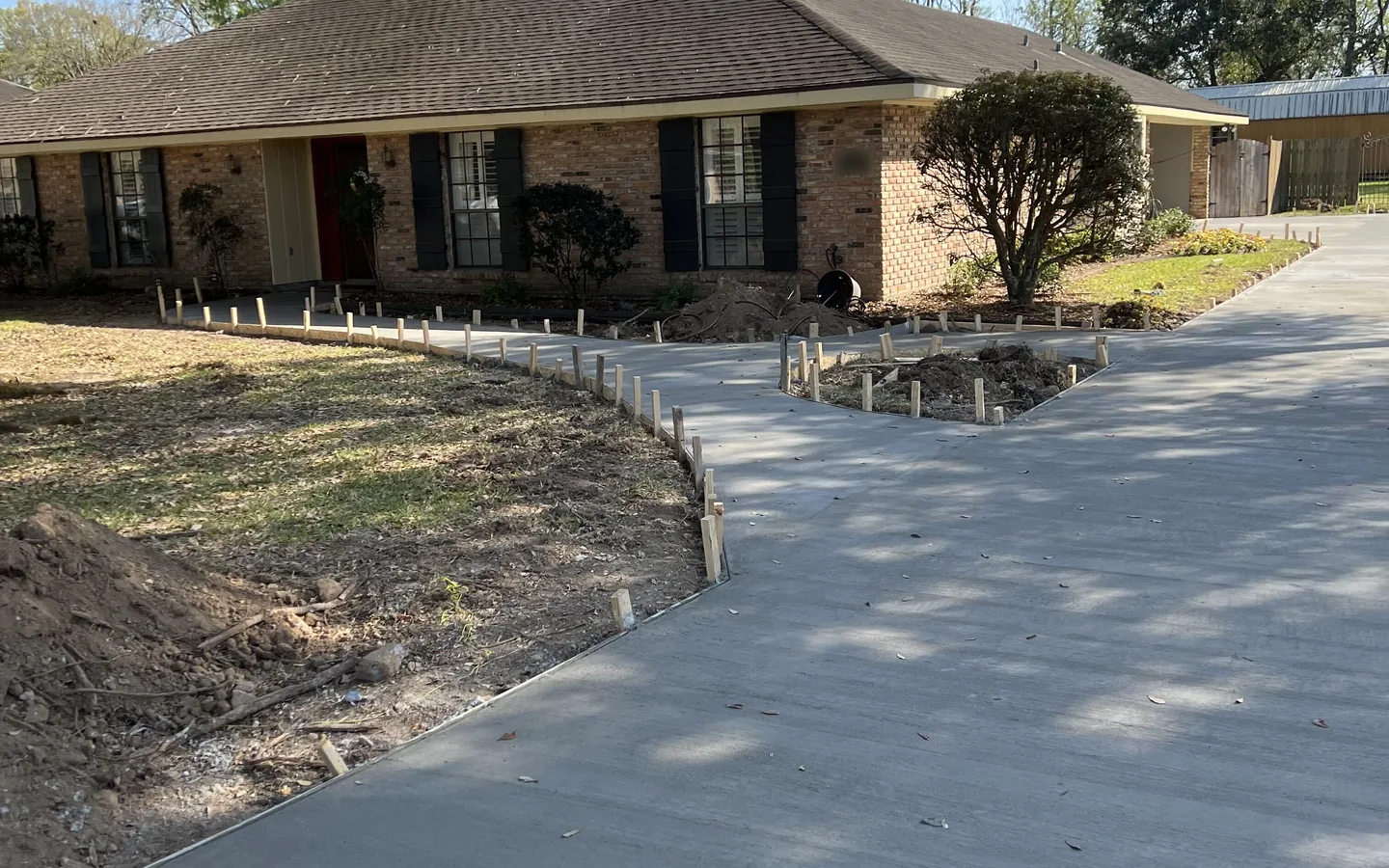 New concrete driveway and walk with form stakes still in place in front of a brick ranch house, concrete driveways