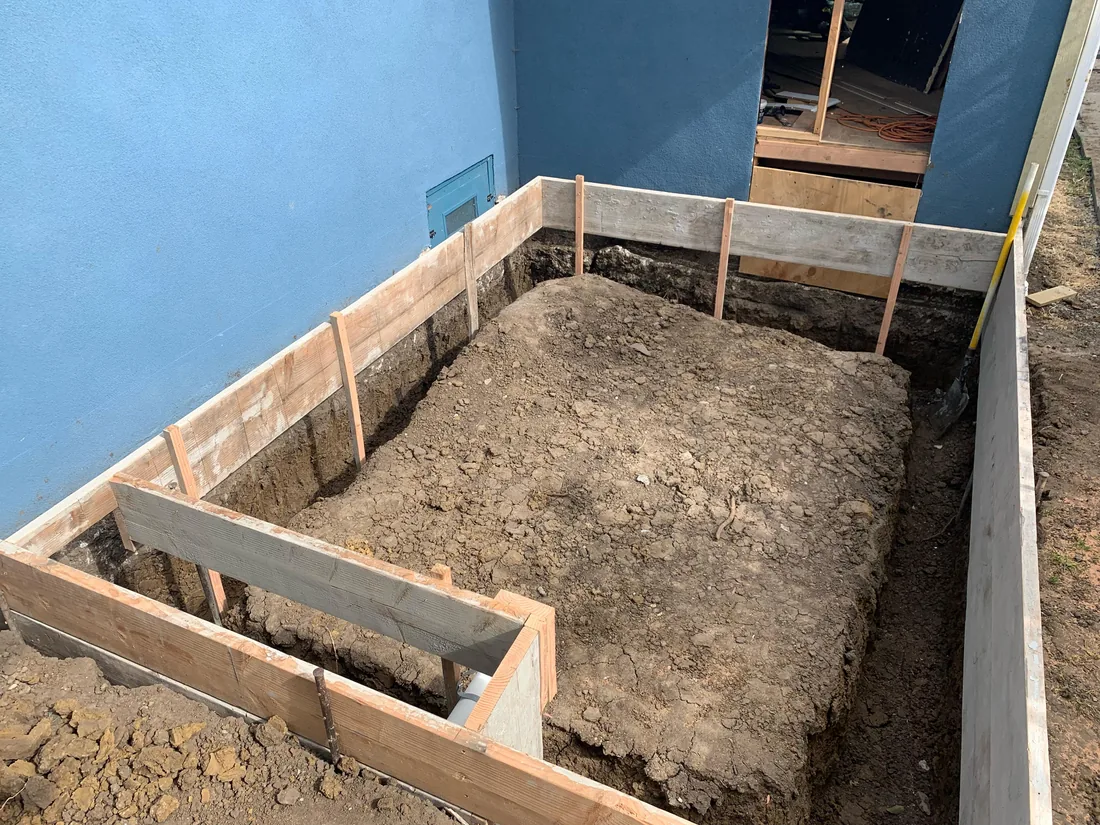 Wood footing forms set around a dug trench for an addition beside a house wall, concrete foundations and footings