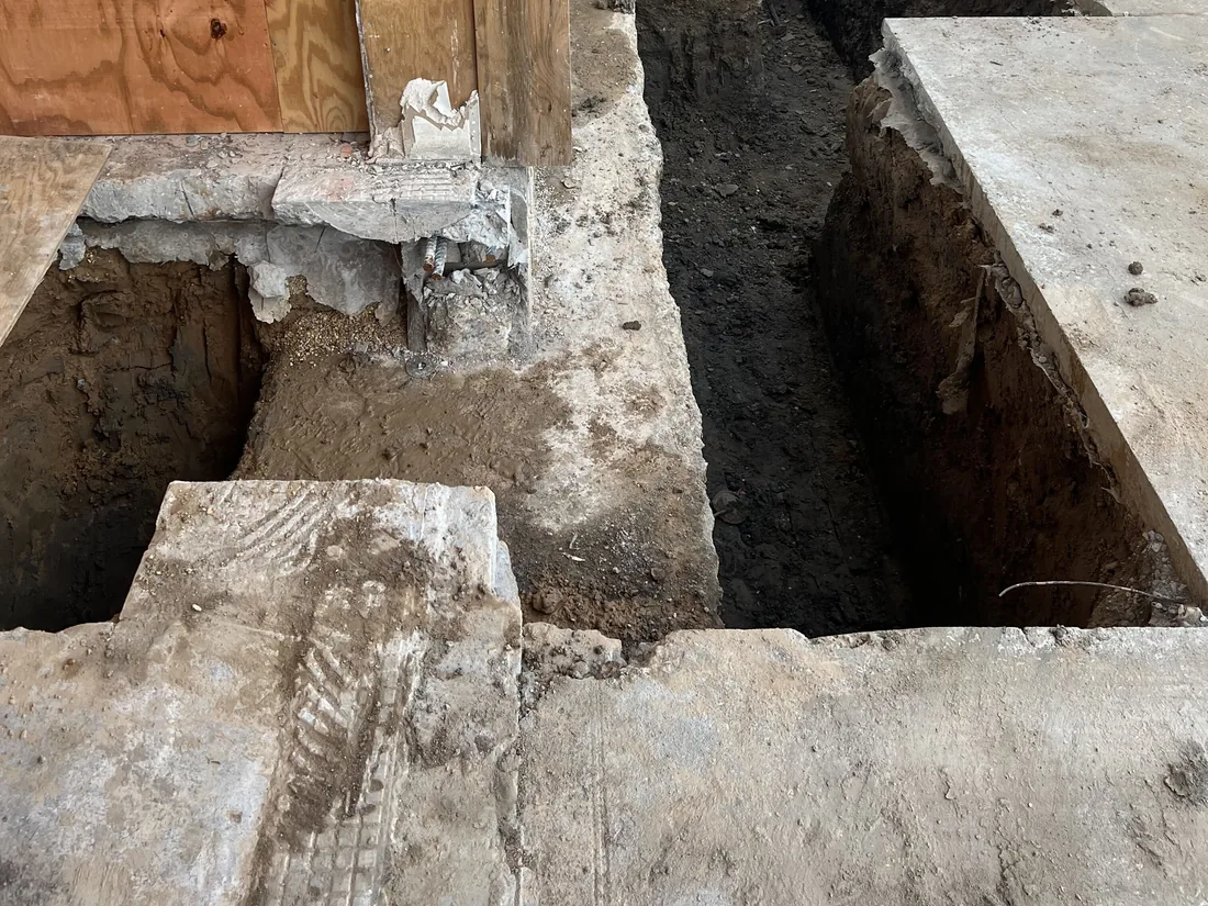 Footing trench dug through an old slab along a wall, with the cut slab edges and plywood forms exposed, concrete foundations and footings
