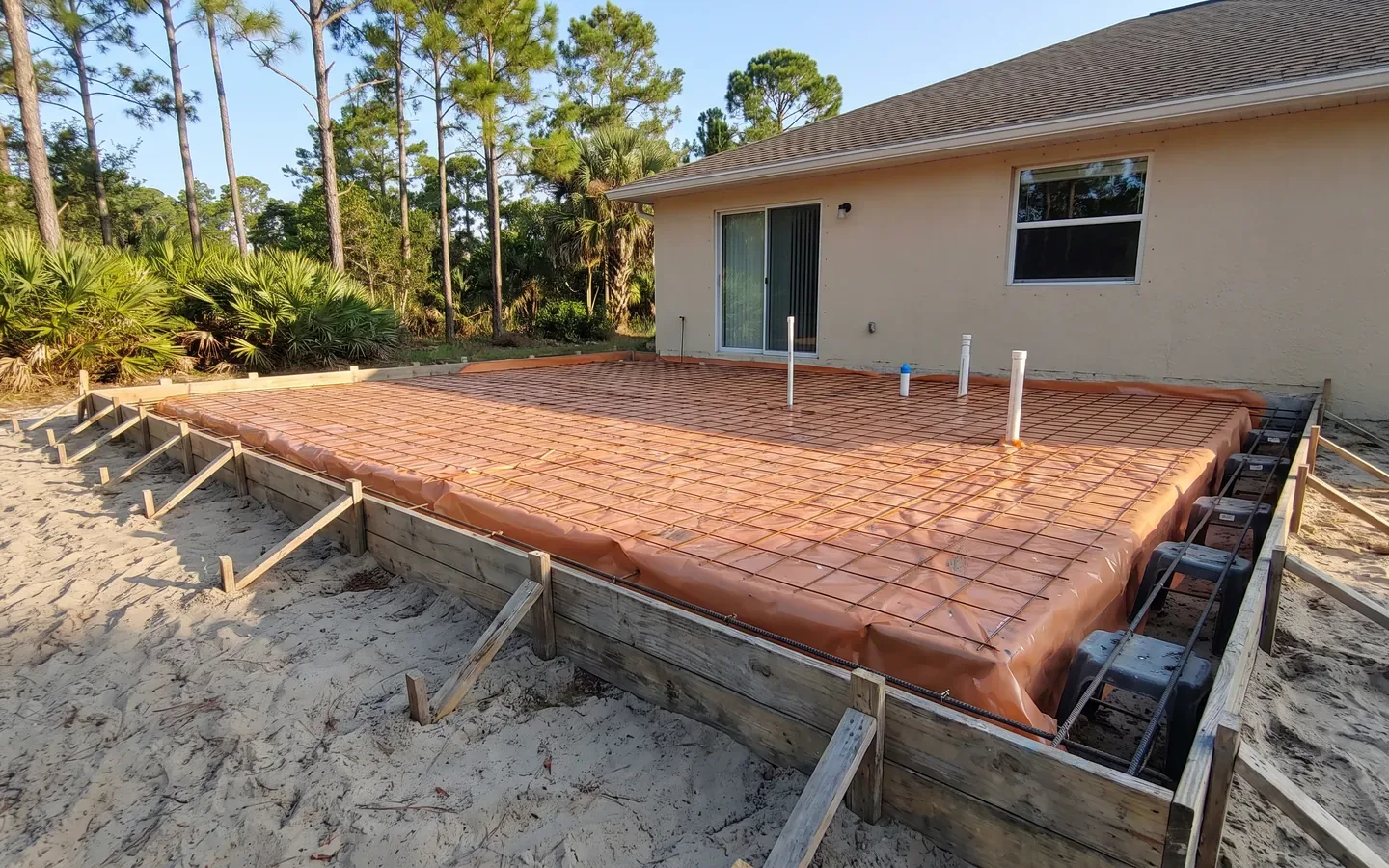 House addition slab ready to pour, with vapor barrier, rebar on chairs, plumbing stub-outs and wood forms, concrete foundations and footings