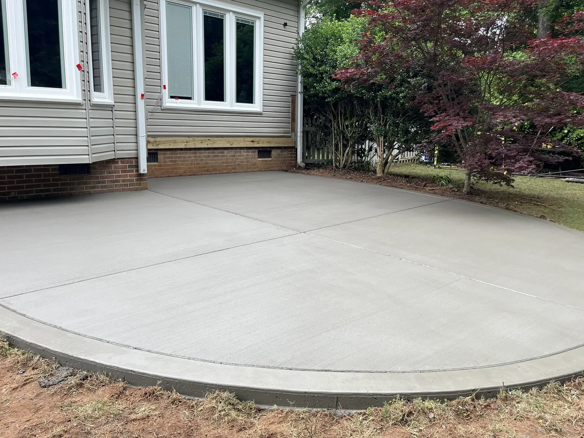 Curved broom-finish concrete patio with control joints behind a house, bordered by lawn, concrete patios and walkways
