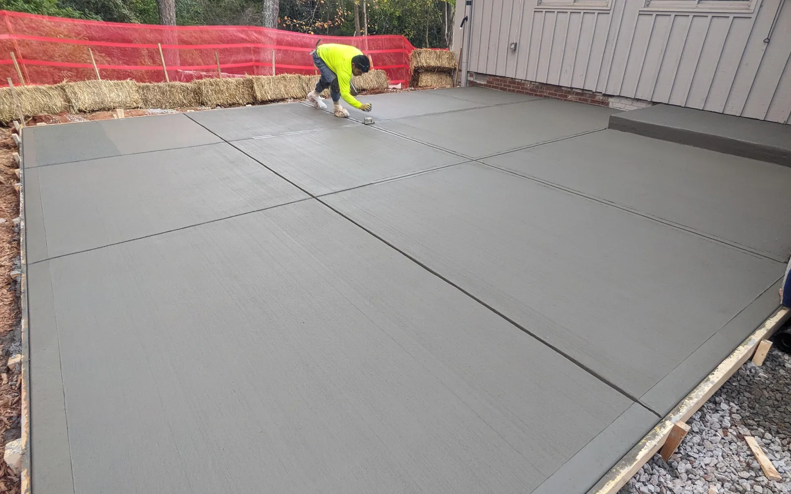 Worker tooling a joint in a new broom-finish concrete patio with form boards along the edge, concrete patios and walkways