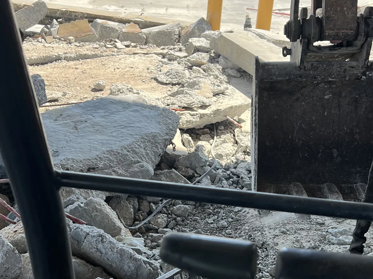 Excavator bucket pulling up slabs of broken concrete, seen from inside the cab, concrete removal and replacement