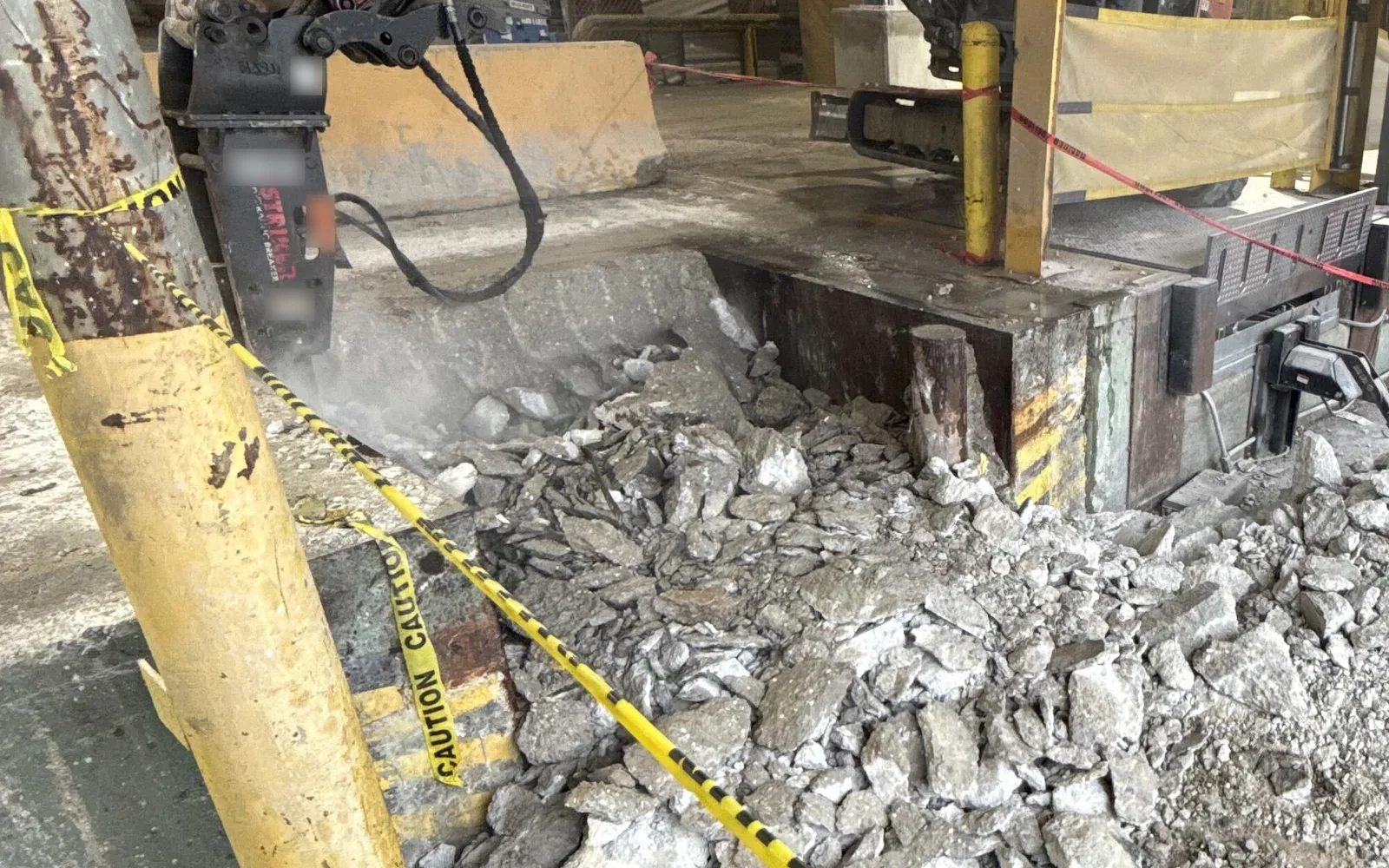Hydraulic breaker on a mini excavator breaking out a concrete slab, with broken chunks piled below, concrete removal and replacement