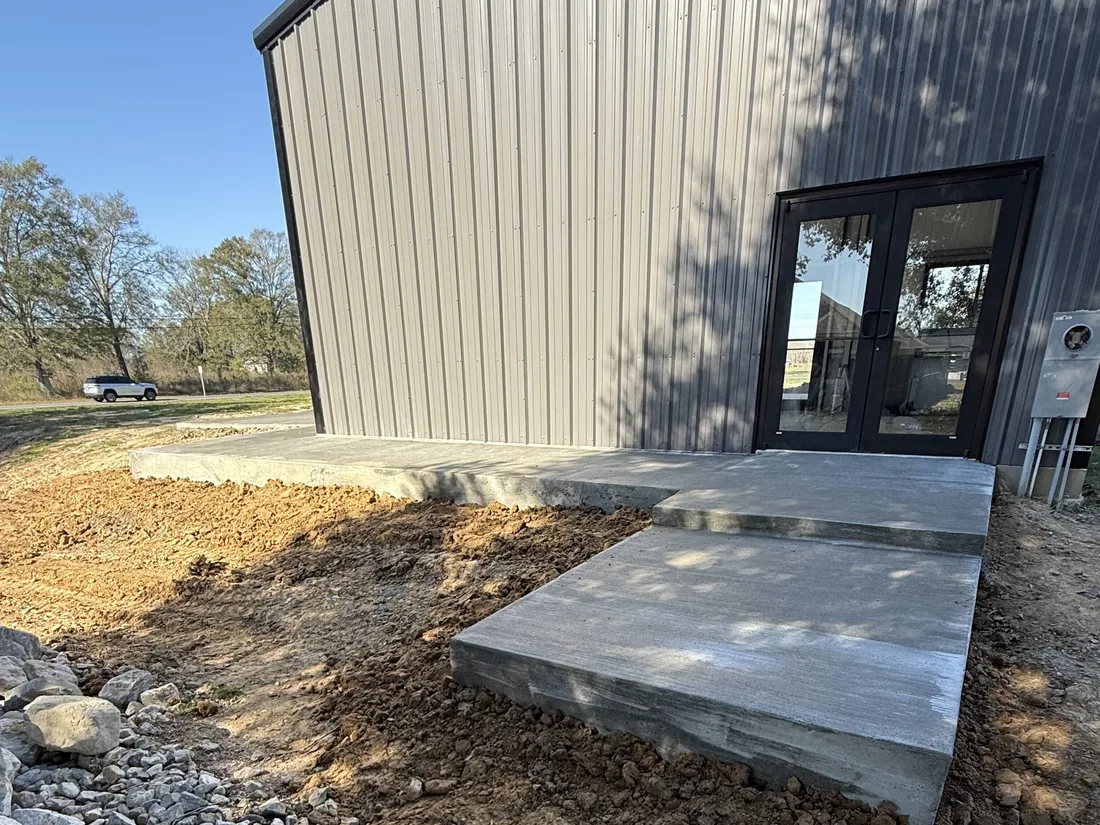 New concrete landing and step pad at the glass double doors of a metal building, concrete slabs and pads