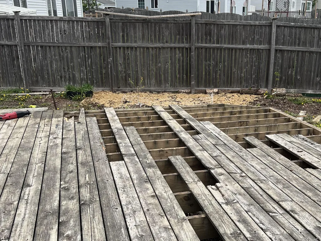 Backyard deck with rows of boards pried off and the joists showing, partway through the tear-out, demolition