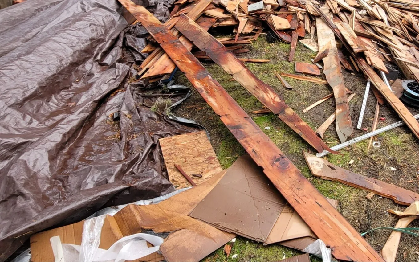 Old deck boards torn out and piled on tarps and cardboard in a backyard, demolition