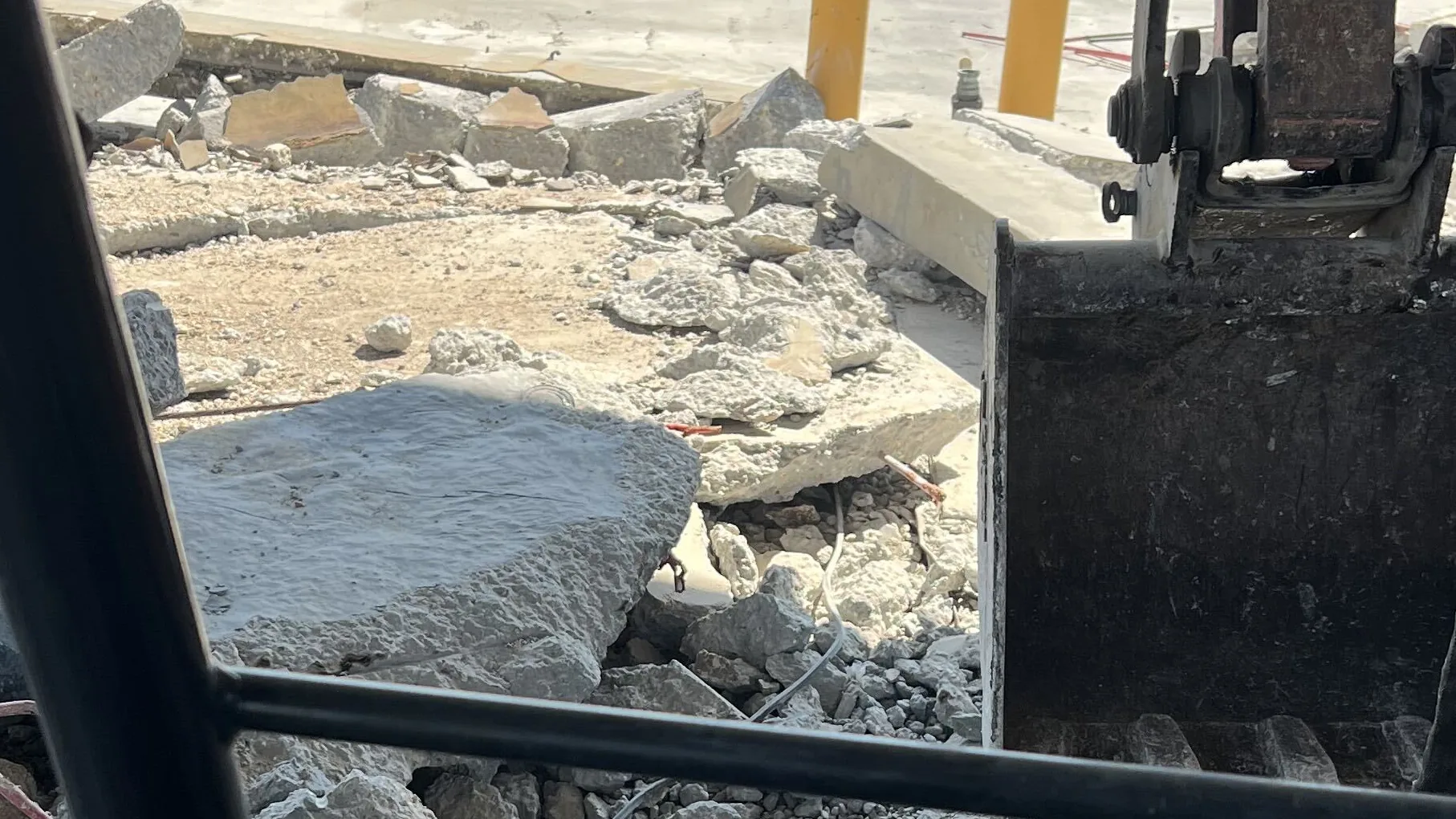 Broken concrete slab pieces and an excavator bucket seen from inside the cab, concrete removal and replacement