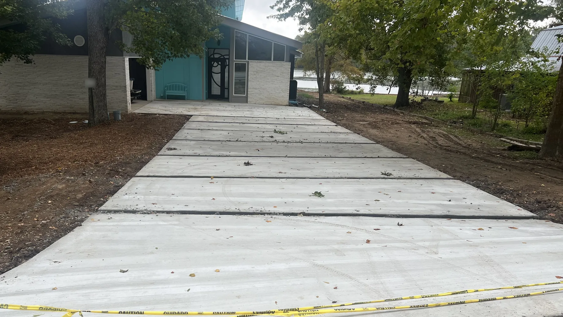 New broom-finish concrete driveway with control joints running up to a one-story house under mature oaks, concrete driveways