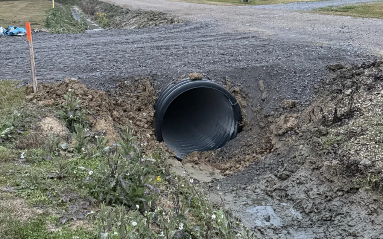 New corrugated culvert pipe laid in a roadside ditch where a driveway crosses, with water in the ditch, yard drainage